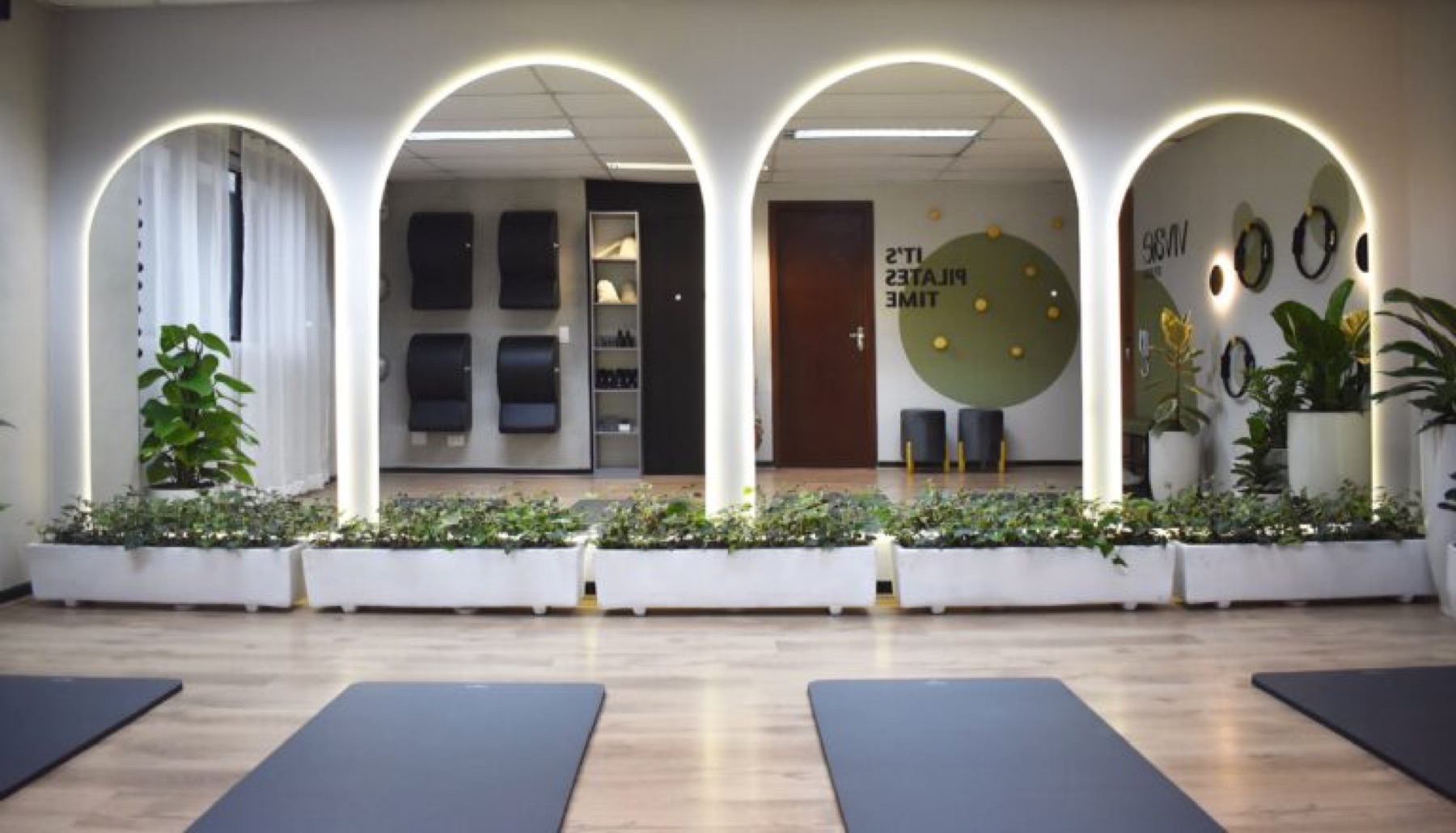 Sala principal do Studio Vivae com arcos iluminados, plantas e mats de Pilates